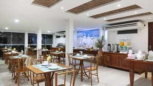A spacious dining area with wooden tables and chairs, a kitchen area with a coffee machine, and a large painting on the wall. - Pousada Bahia 10 (Morro de Sao Paulo)