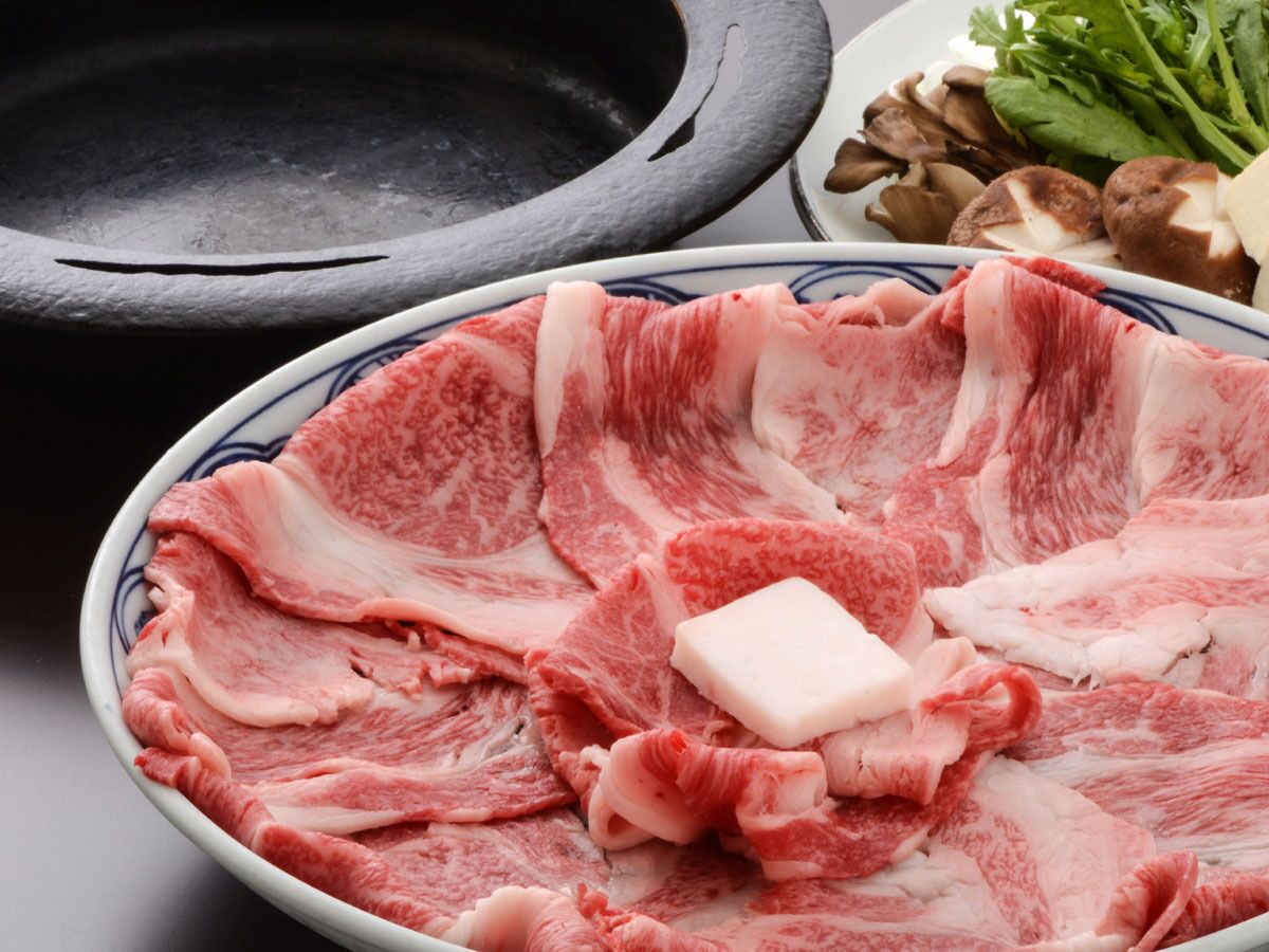 A bowl of raw meat with a piece of butter on top, a stone cooking surface, and some mushrooms.