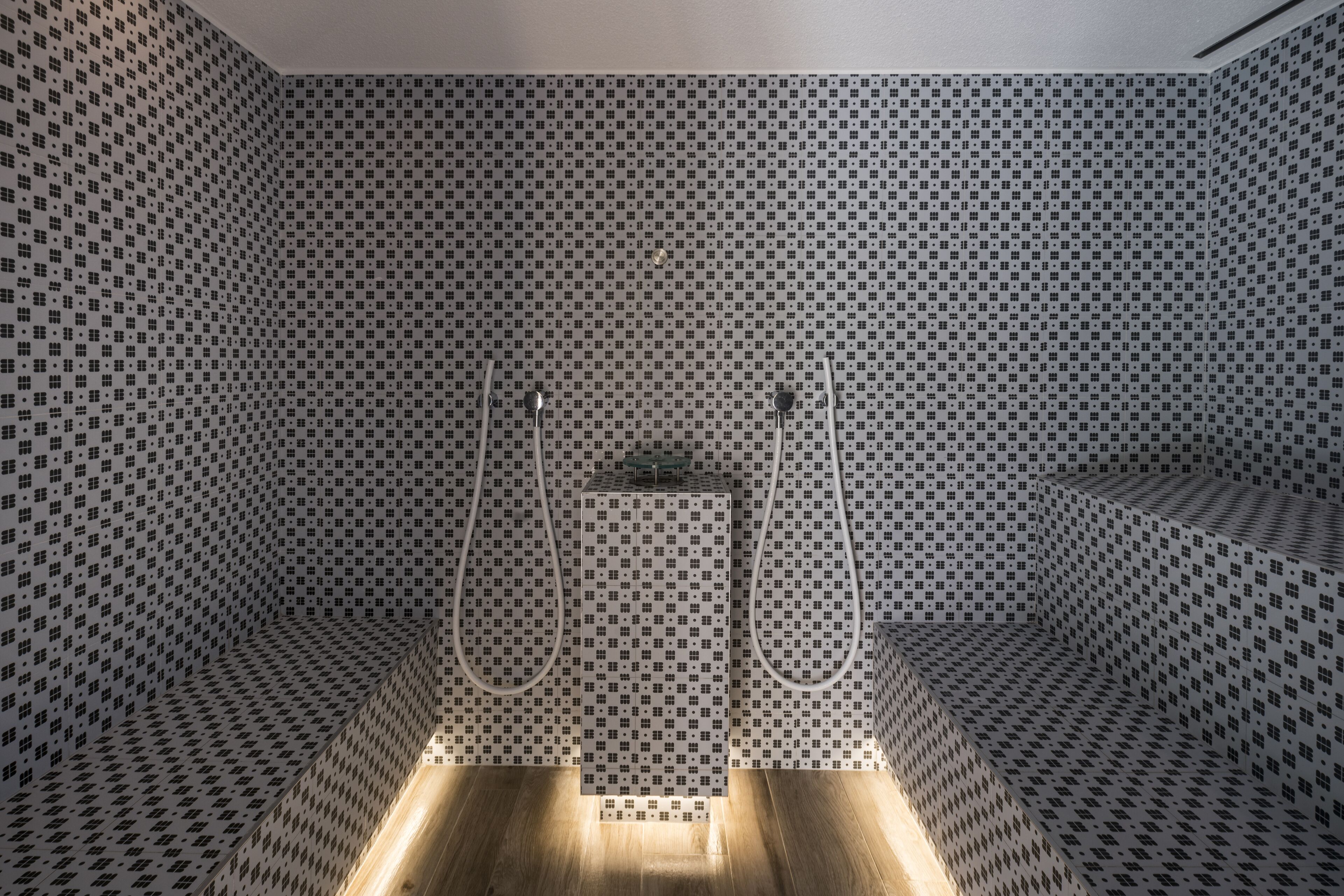 Een moderne badkamer met een betegeld vloertapijt in ruitpatroon, een centraal geplaatst wastafelmeubel en twee douchekoppen.