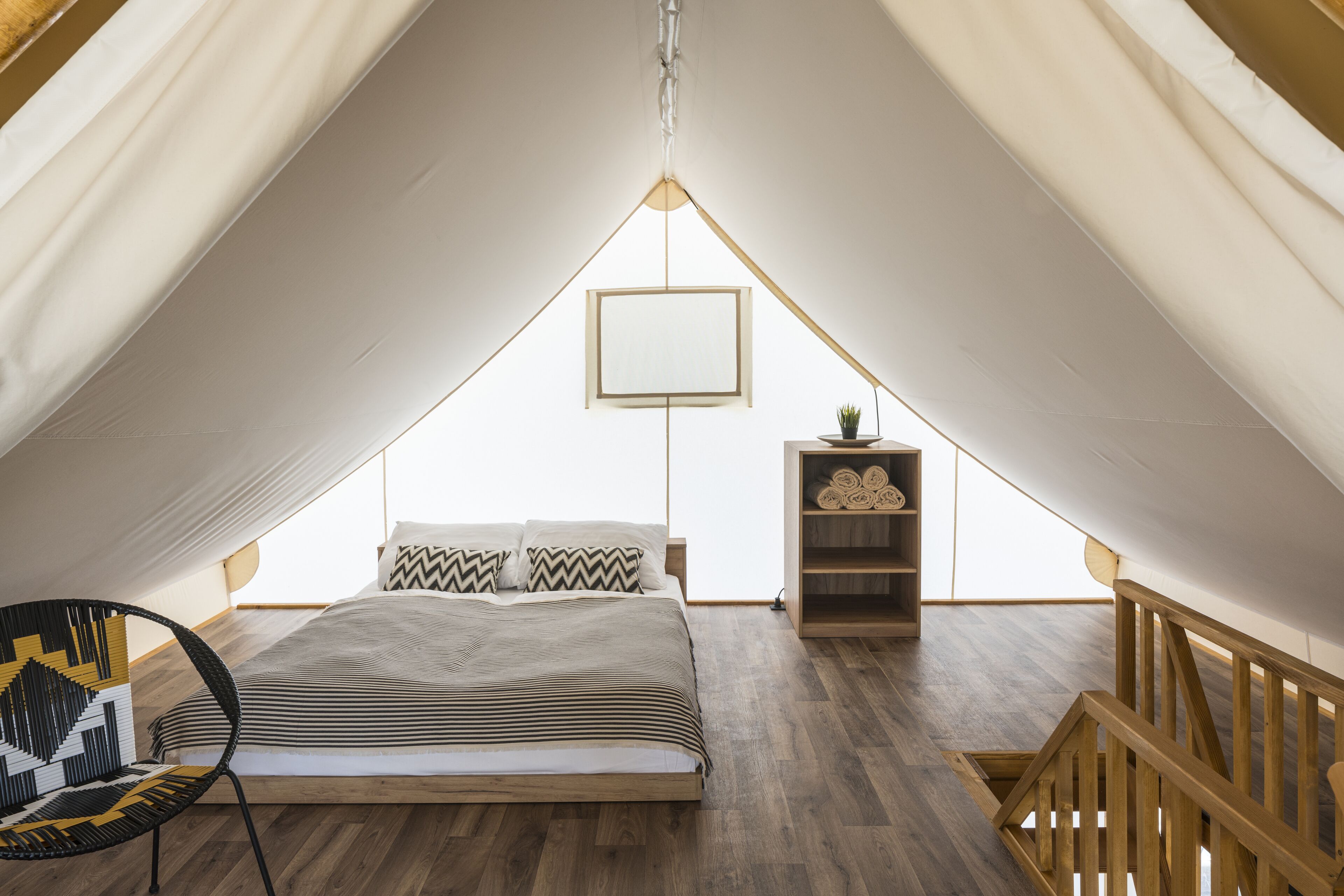 Une chambre à coucher avec un lit, une chaise, une table de chevet ornée d’une plante et une rambarde en bois.