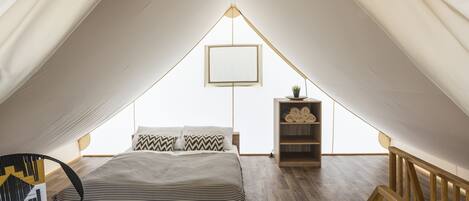 A bedroom with a bed, a chair, a bedside table with a plant, and a wooden railing.
