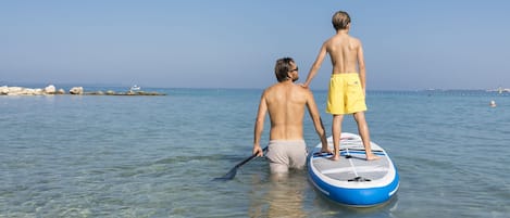 Two people standing on a paddleboard in clear shallow water.