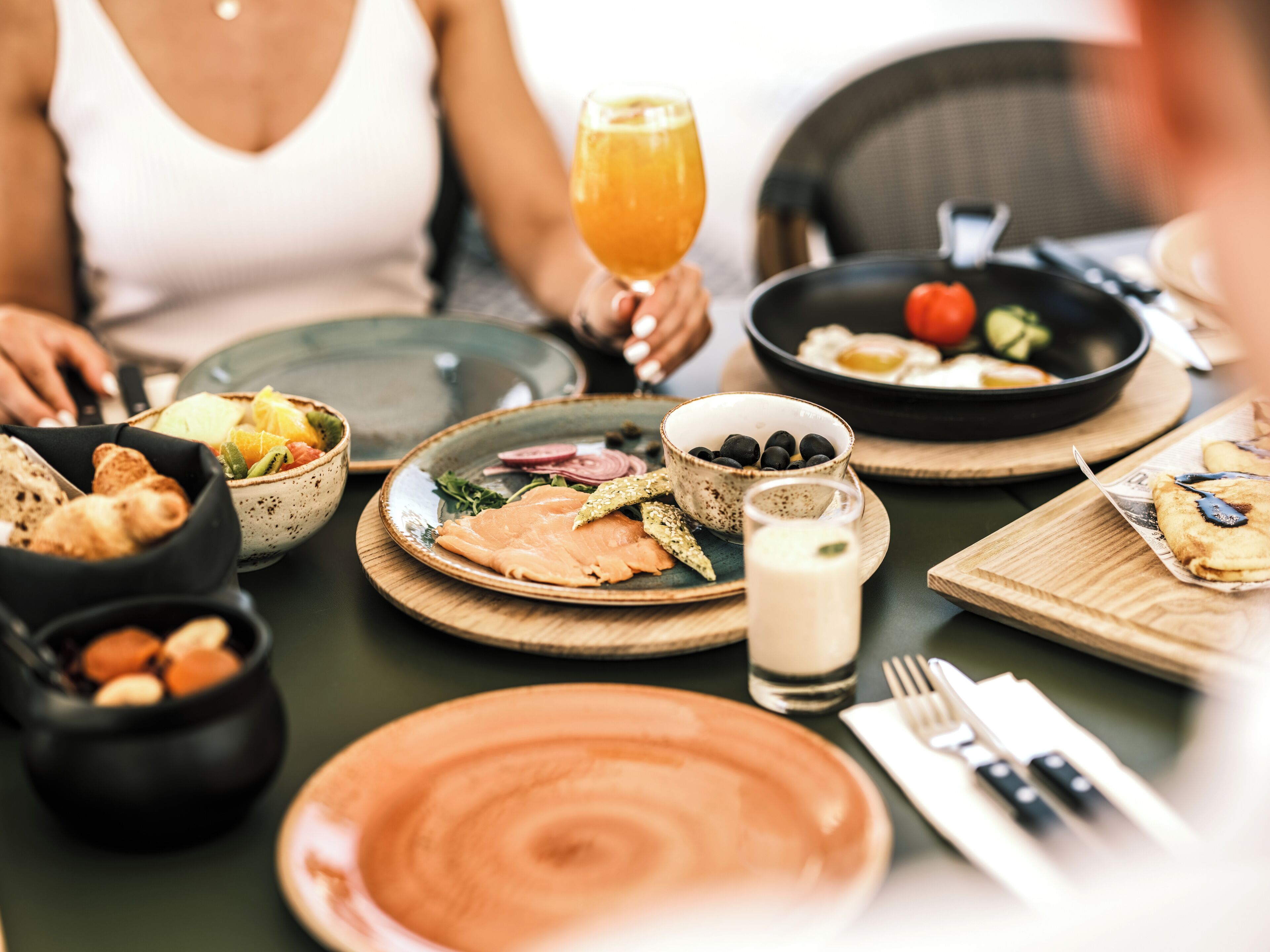 Una mesa de comedor con varios platos, incluyendo un bol de aceitunas, un plato de salmón y un vaso de zumo de naranja.