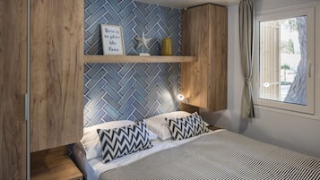 A bedroom with a herringbone-patterned wall, a bed with striped bedding, a nightstand, a shelf with decorative items, and a window with curtains.
