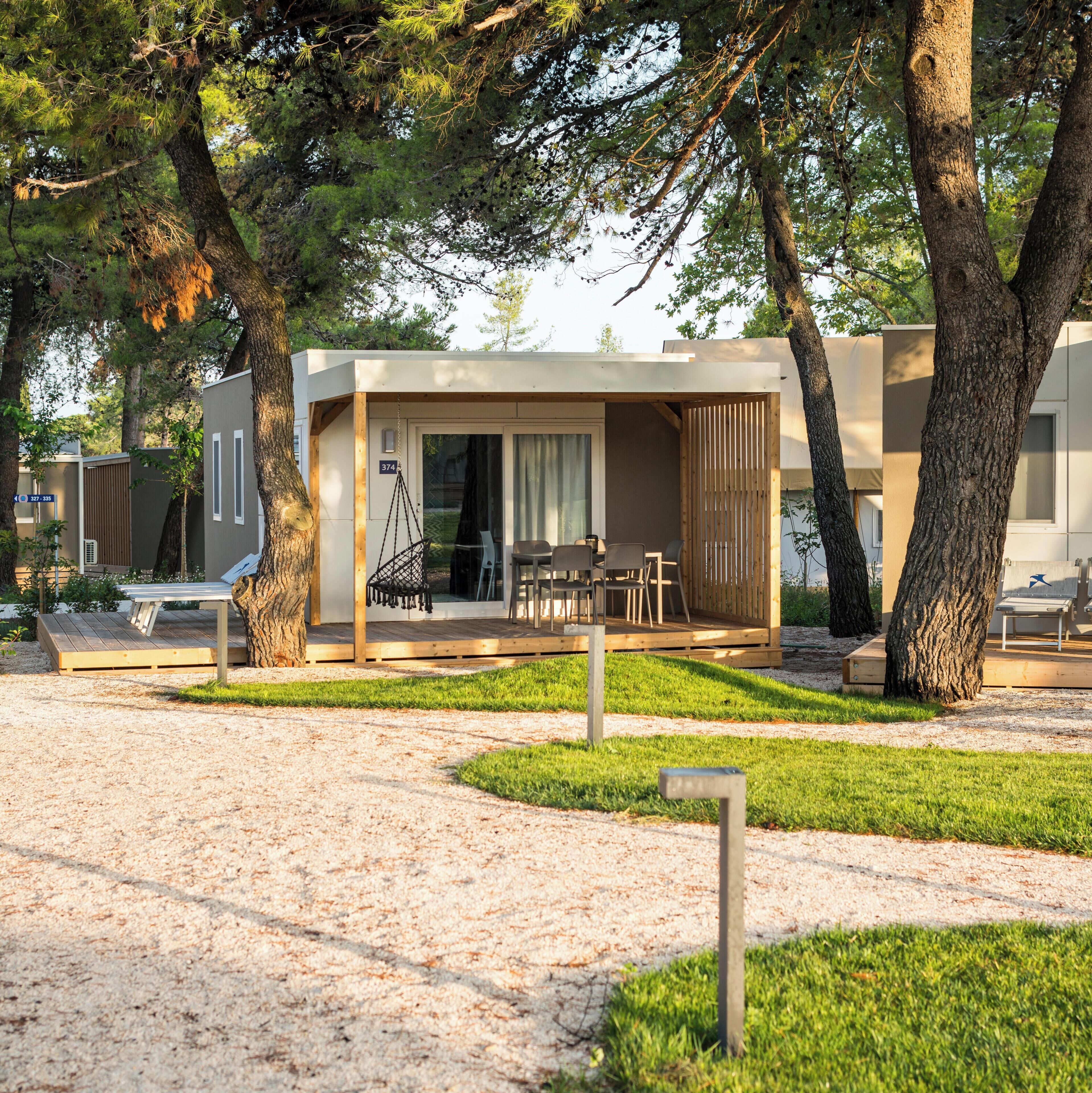 A modern outdoor seating area with a wooden deck, a swing, and a covered seating space with chairs and a table.