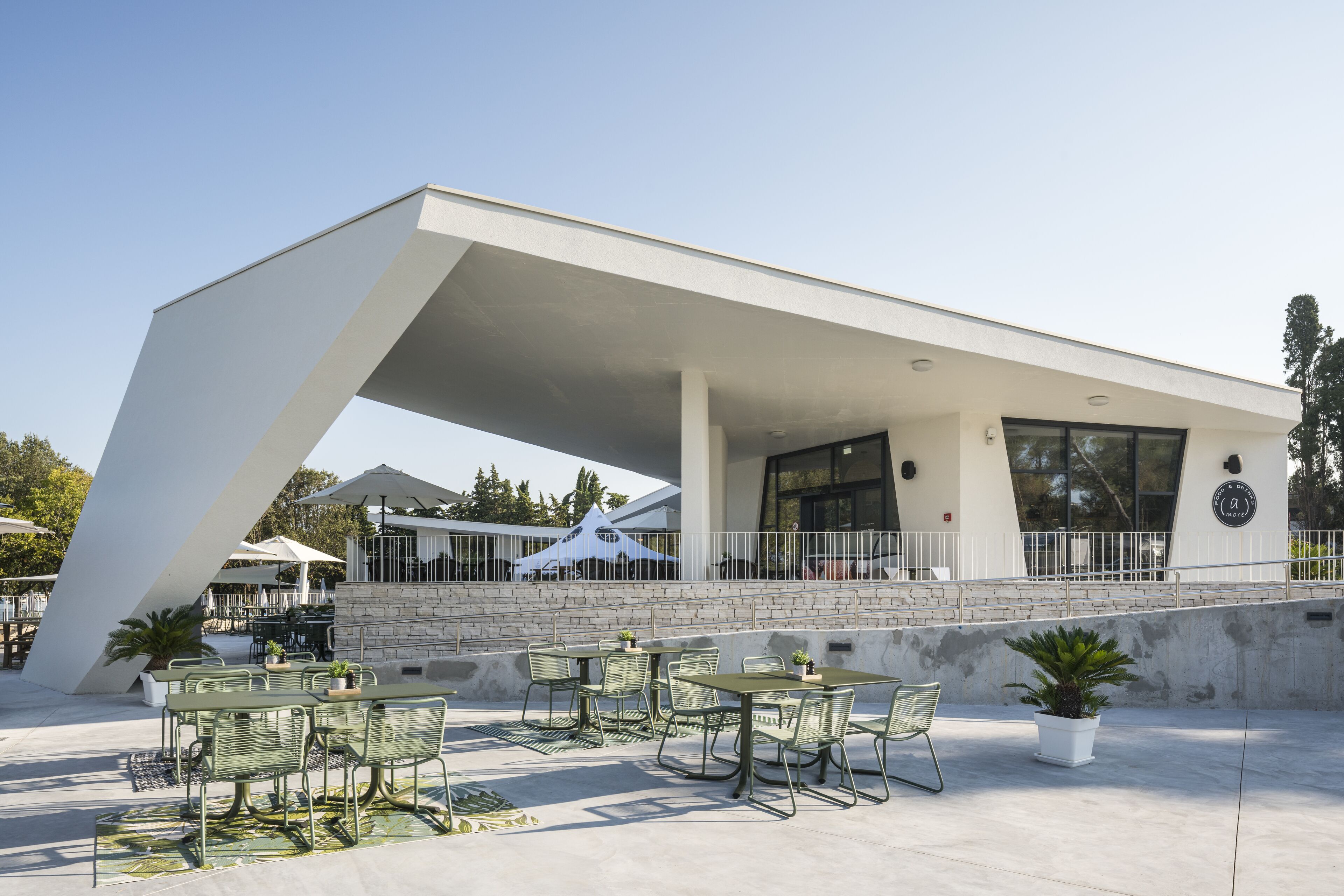 Un patio al aire libre con mesas y sillas, un edificio blanco con techo inclinado y una pared de piedra.