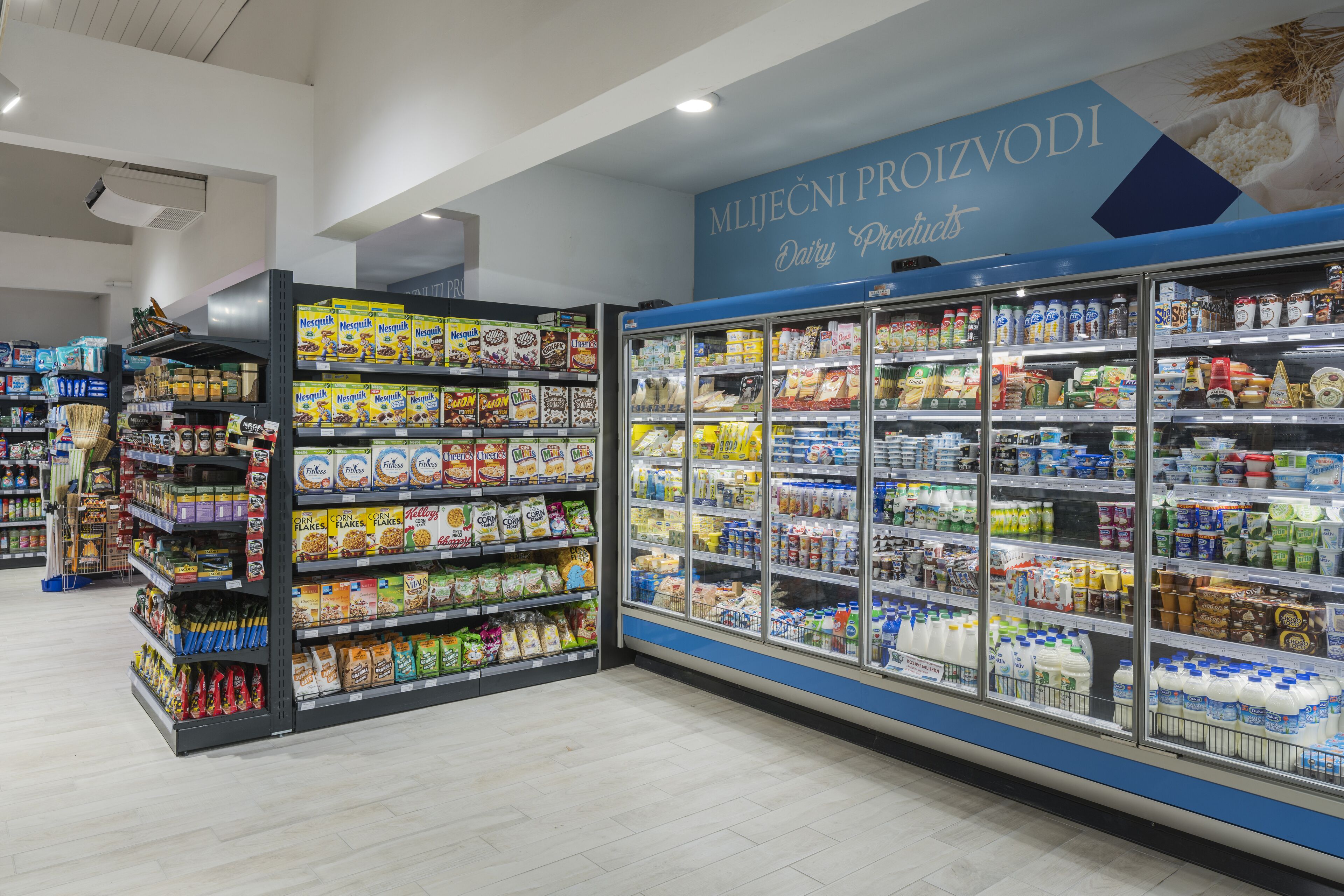 Un pasillo de supermercado con cereales y productos lácteos en estantes y refrigeradores.