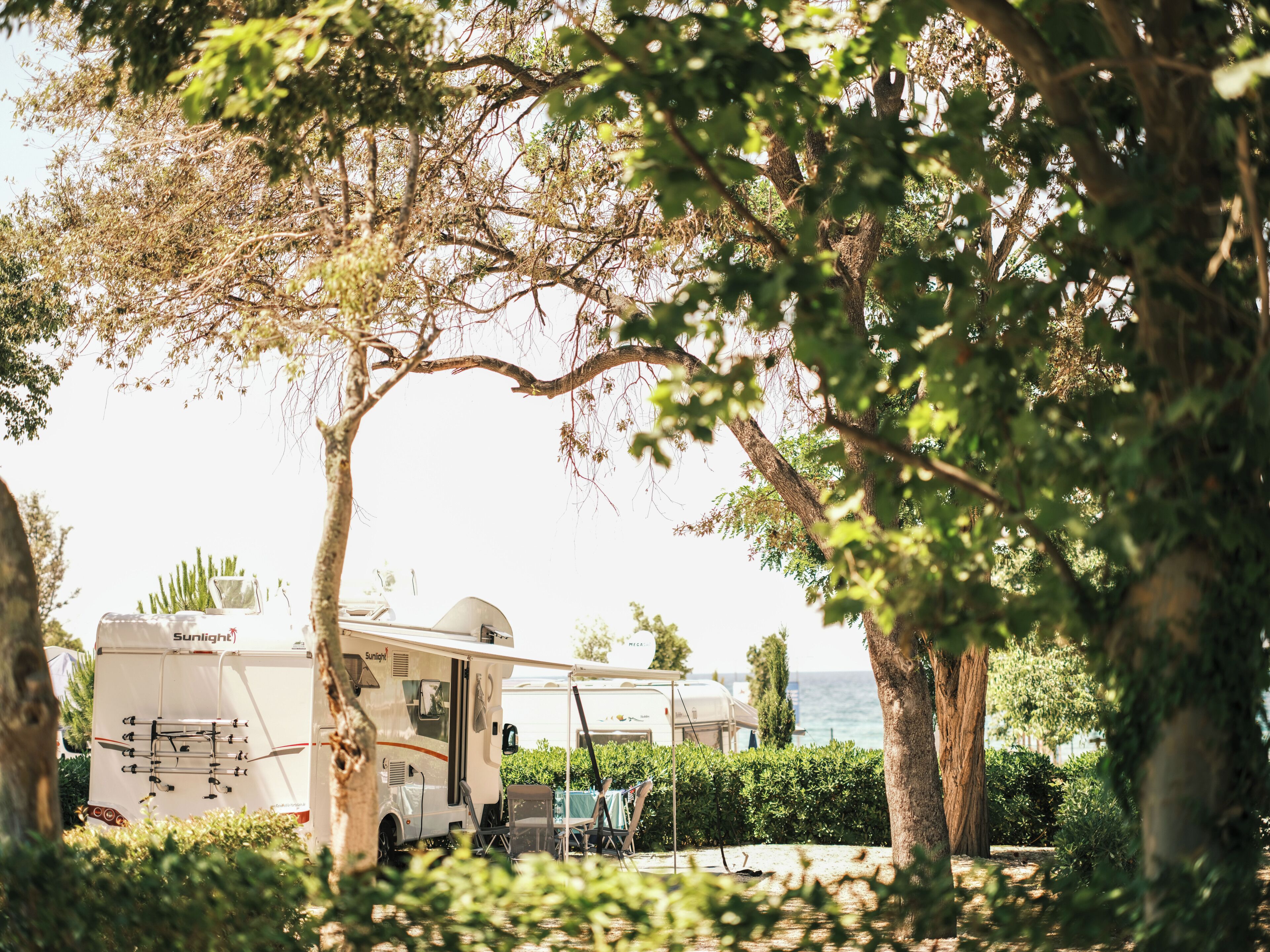A recreational vehicle (RV) parked in a shaded area with trees, a table, and chairs.