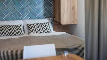 A bedroom with a bed, pillows, a nightstand, a wooden table, and a wall with a herringbone pattern.