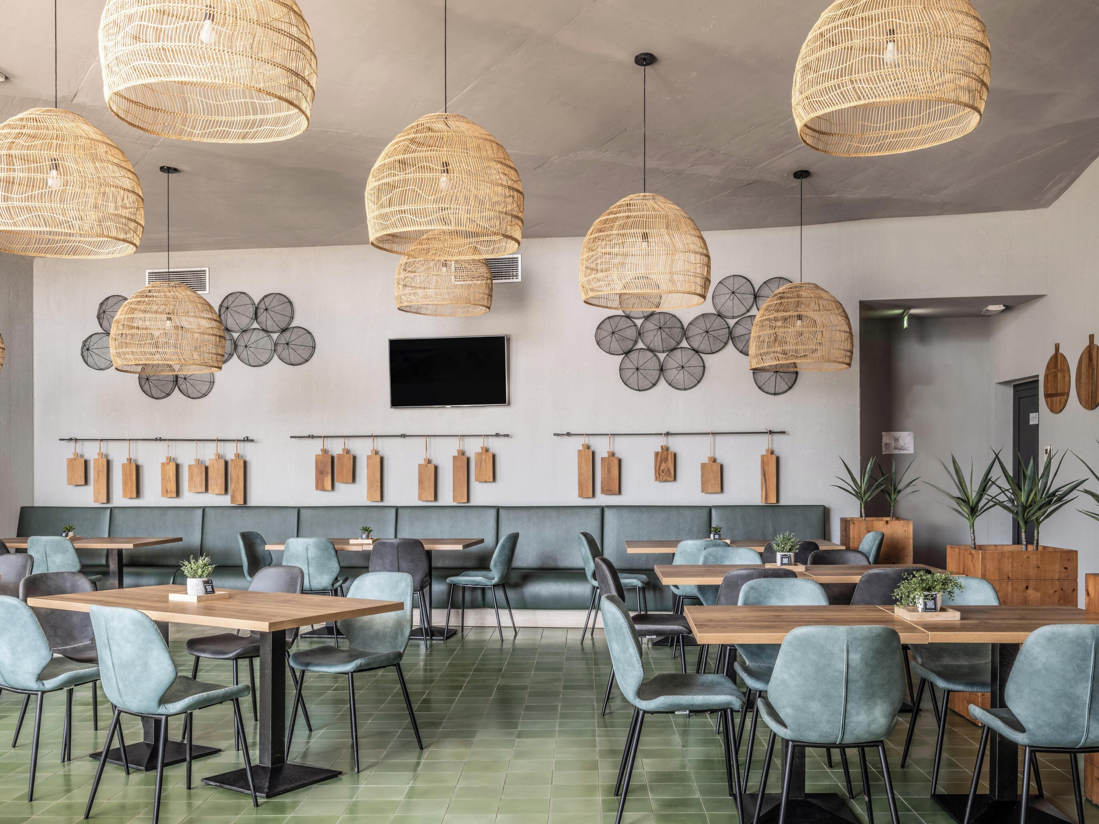 Un espace repas moderne doté de plusieurs tables et chaises, de luminaires suspendus en osier, d’un téléviseur à écran plat et de jardinières en bois fixées au mur.