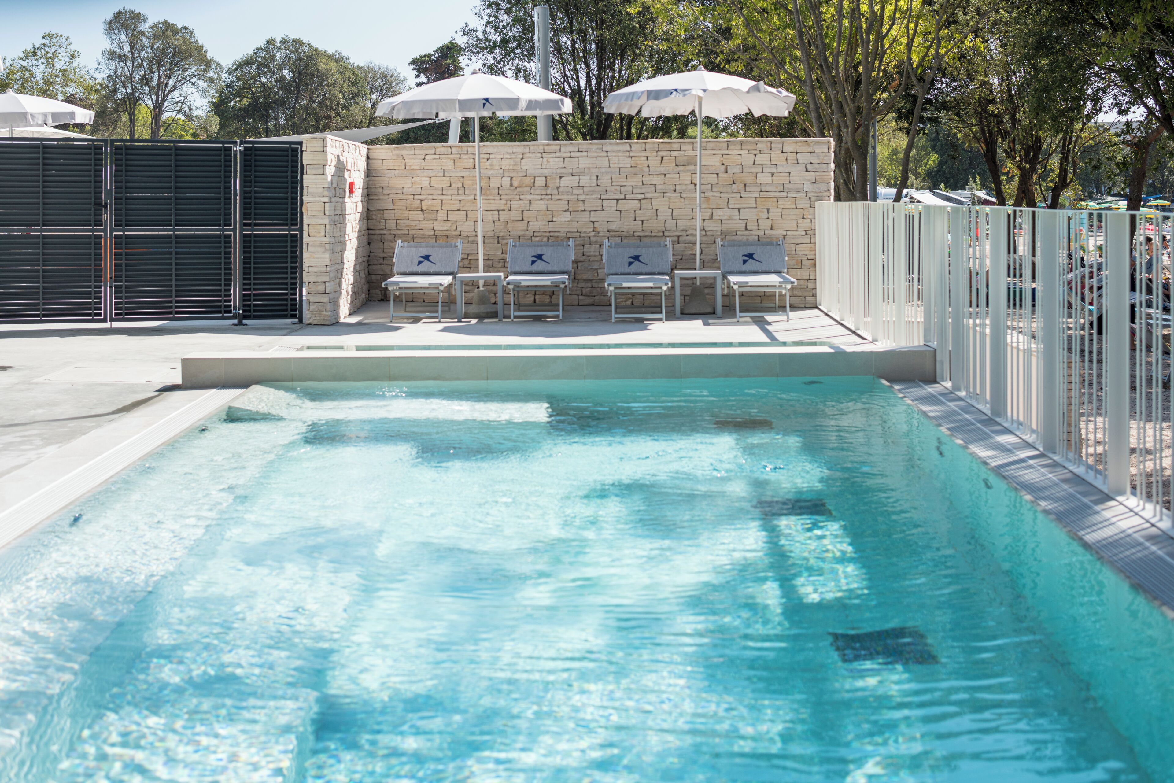Une piscine à l’eau claire, entourée d’un mur de pierre et agrémentée de parasols blancs et de chaises longues.