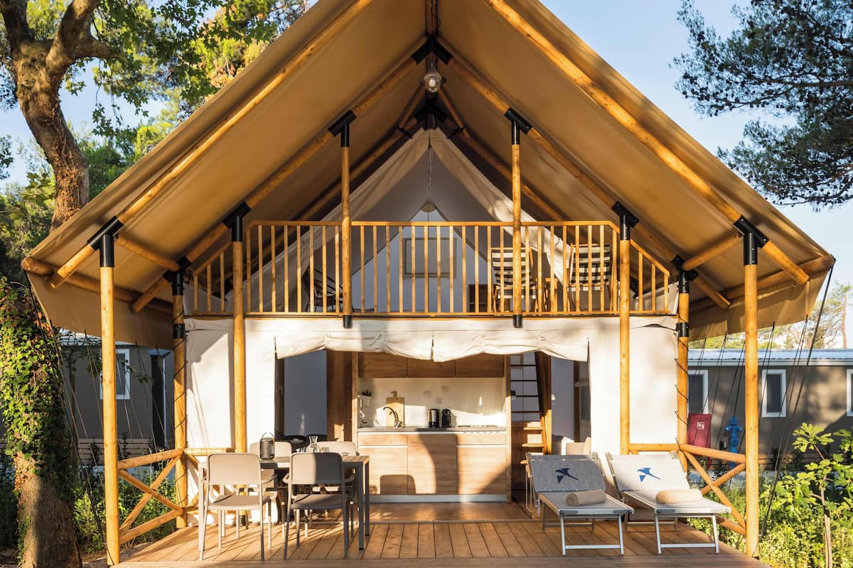 Une cabane en bois dotée d’un balcon, d’un espace extérieur aménagé pour s’asseoir et d’un coin cuisine.