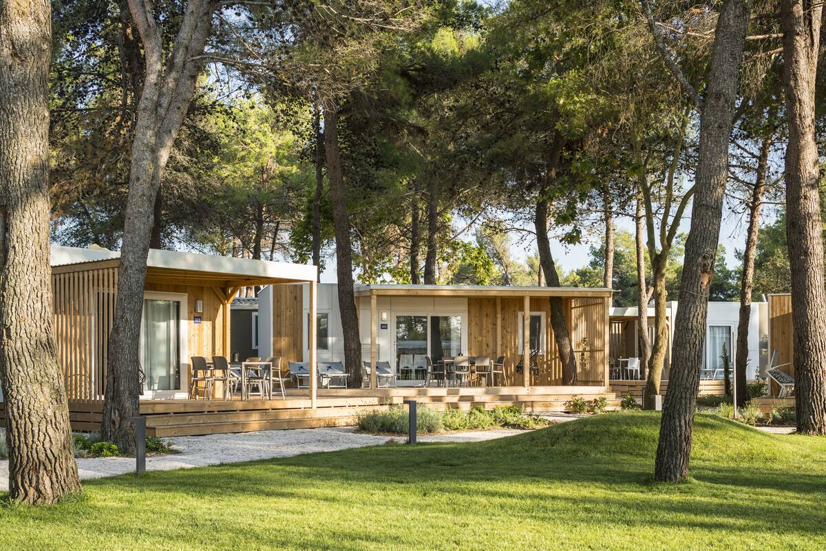 Un bâtiment moderne de style cabane en bois, doté de nombreuses pièces, d’un espace extérieur couvert avec des sièges et d’une pelouse bien entretenue.