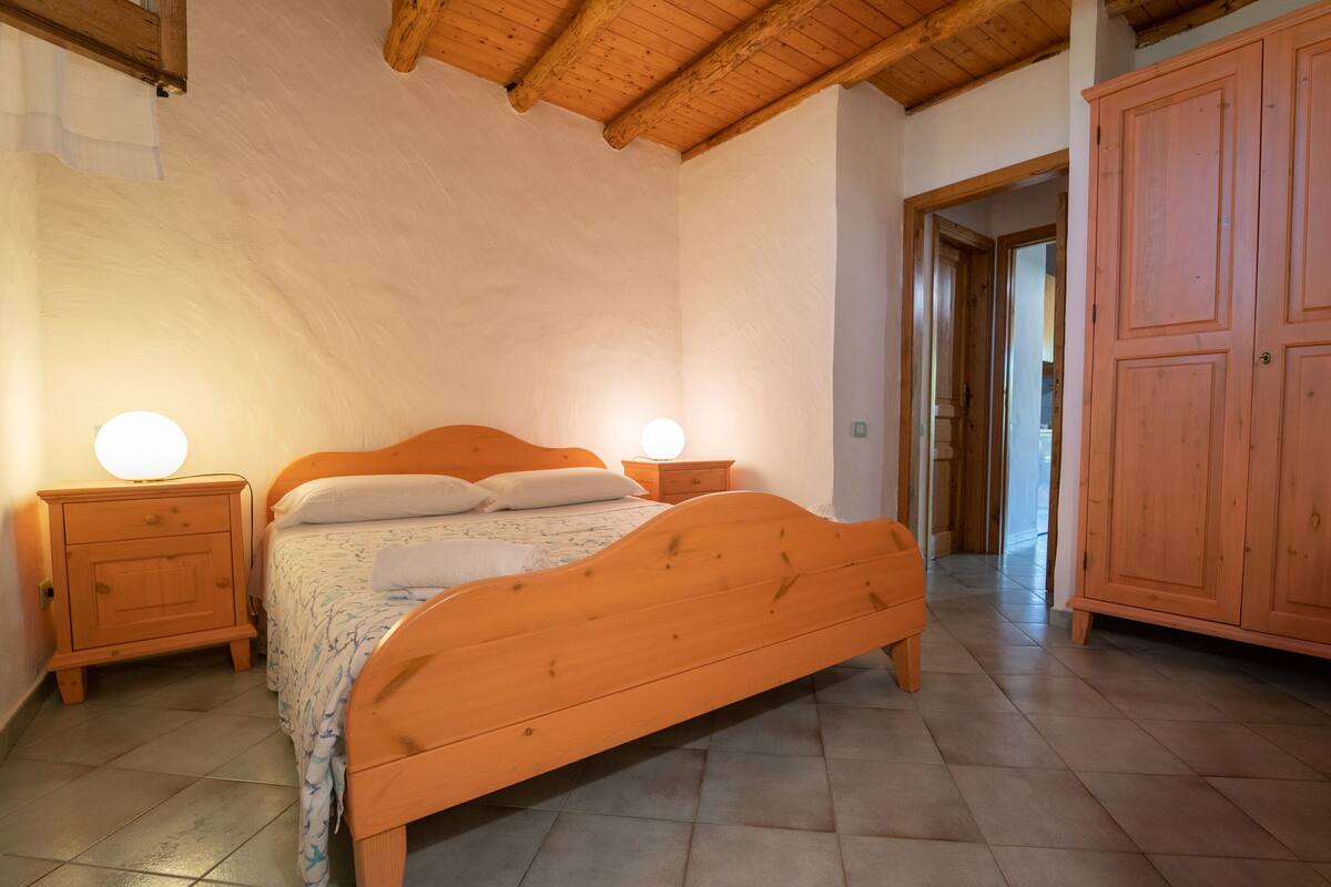 Quarto com cama de madeira, duas mesas de cabeceira e um guarda-roupa.
