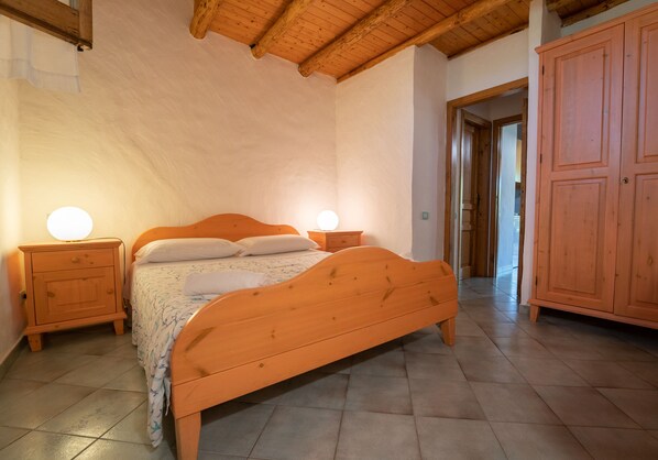 A bedroom with a wooden bed, two bedside tables, a wardrobe, and a tiled floor. - Agriturismo Hibiscus (Ustica)