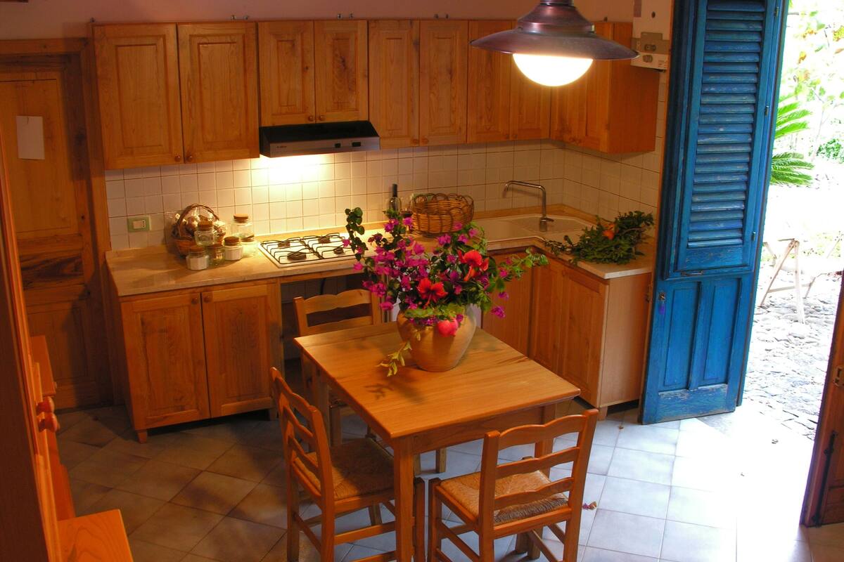 Uma cozinha com armários de madeira, painel de azulejos, fogão a gás, pia e mesa de jantar com cadeiras.