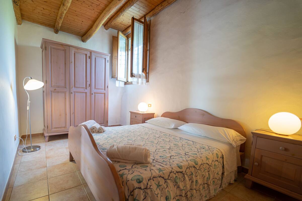 Quarto com cama de madeira, luminárias de cabeceira, guarda-roupa e uma janela.