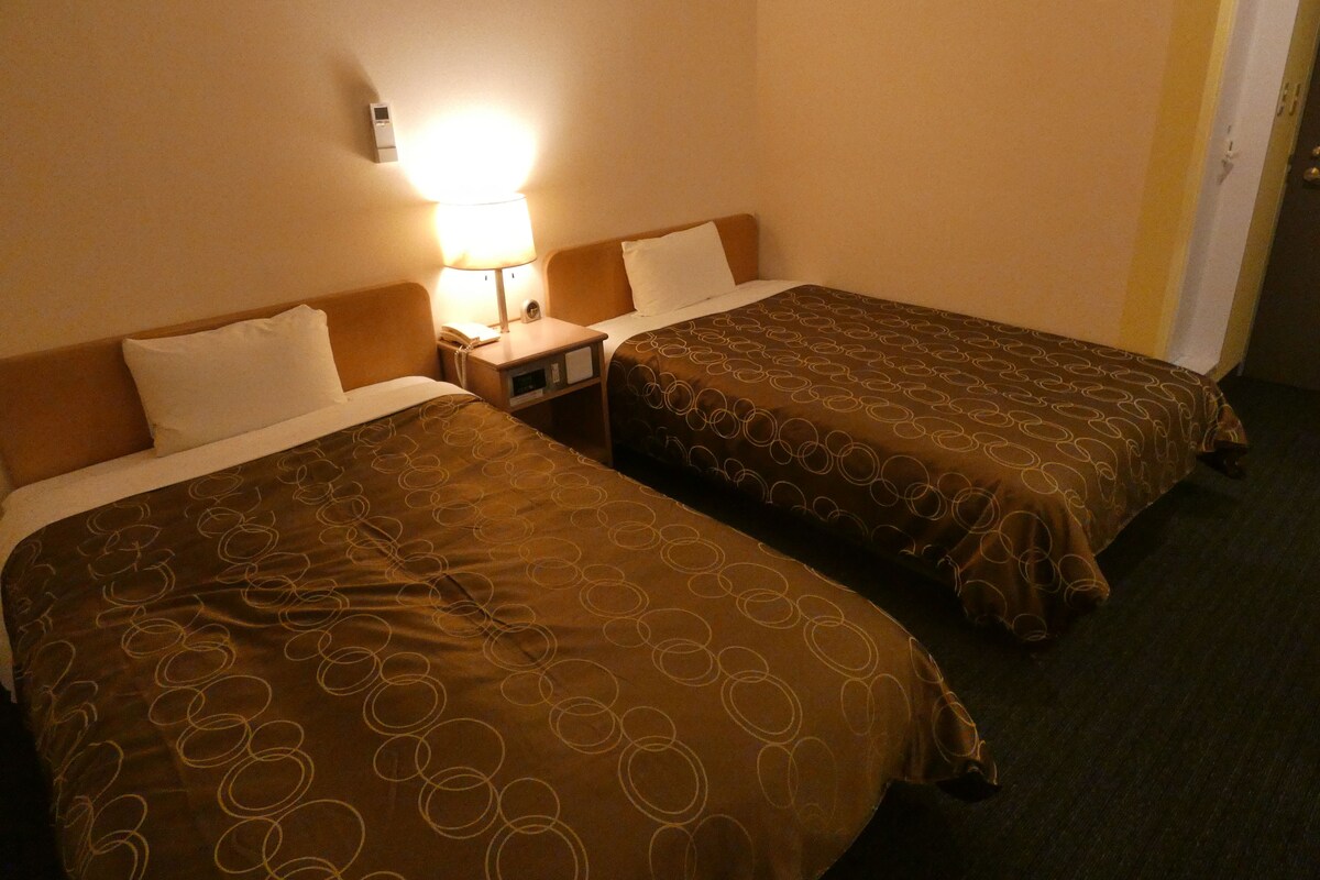 Habitación de hotel con dos camas, una mesita de noche y una lámpara fijada a la pared.