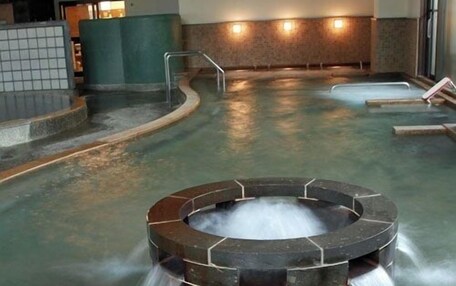 A hot tub with a circular stone design surrounded by a pool, with steps leading into the water.