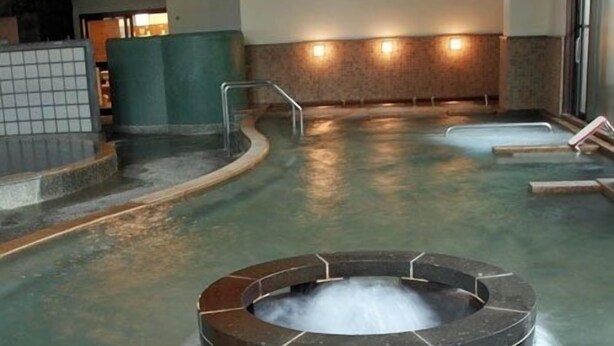 Een hottub met een rond steenmotief, omringd door een zwembad, met treden die naar het water leiden.