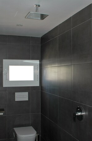A modern bathroom with dark tiles, a toilet, a shower, and a window. - Jingtu Wellness & Spa Resort (Comares)