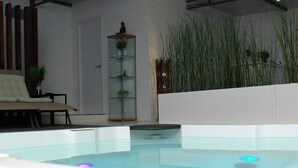A modern indoor pool area with a glass enclosure, a seating area with a sofa, and tall green plants. - Jingtu Wellness & Spa Resort (Comares)