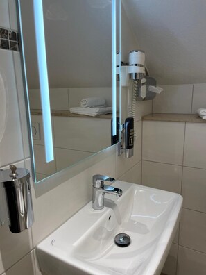 Ein Badezimmer mit weißem Waschbecken, einem Spiegel, einem Handtuchhalter und einer Duschbrause.
