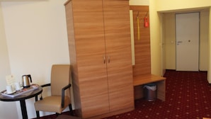 A hotel room with a wardrobe, a small table with a kettle, a chair, a bed, and a carpeted floor. - Harburger HOF (Hamburg)