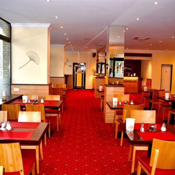 A hotel lobby with a red carpet, wooden furniture, and a wall with a leaf design. - Harburger HOF (Hamburg)