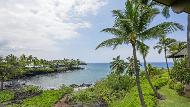 A coastal landscape with a clear view of the ocean, palm trees, and a pathway leading to a building. - Aloha Condos, Kanaloa at Kona, Condo 3703, Oceanfront, AC (Kailua Kona)