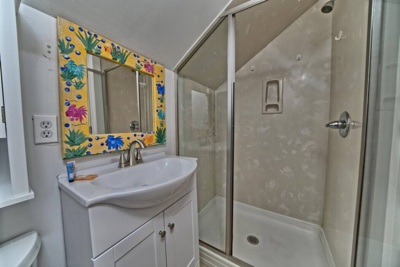 A bathroom with a white sink, a mirror with a colorful floral design, and a shower area with a glass door.