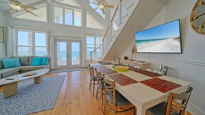 Un vaste espace de vie comprenant une table à manger, un canapé et une vue sur la plage grâce à de grandes fenêtres.