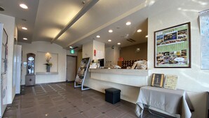 A hotel lobby with a reception desk, a clock, a bulletin board, and a tiled floor.