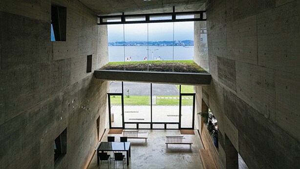 A high-ceilinged interior with a view of a body of water and grassy area outside.