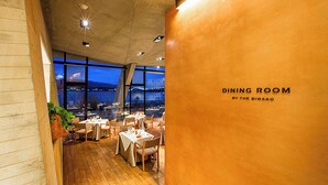 A dining room with tables set for meals, large windows offering a view of the cityscape, and a sign indicating the room is by the Biwako.