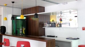 A bar area with red chairs, a counter with a green machine, and bottles on shelves. - Hotel Obino São Borja (São Borja)