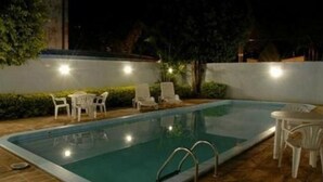 A rectangular swimming pool with a metal ladder, surrounded by white plastic chairs and tables. - Hotel Obino São Borja (São Borja)