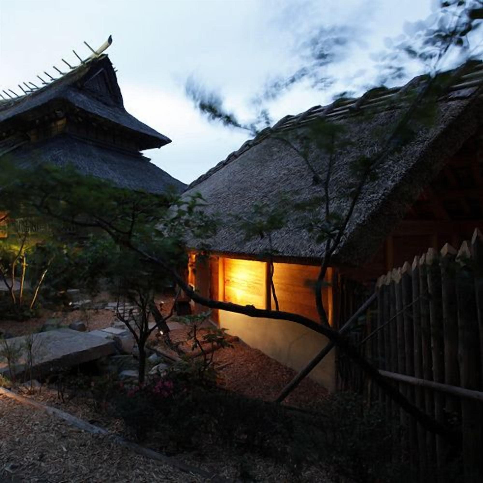 A traditional Japanese building with a thatched roof and wooden structure, surrounded by a garden with rocks and sparse vegetation.