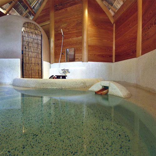 A spa area with a stone hot tub, wooden ceiling beams, and a large arched door.