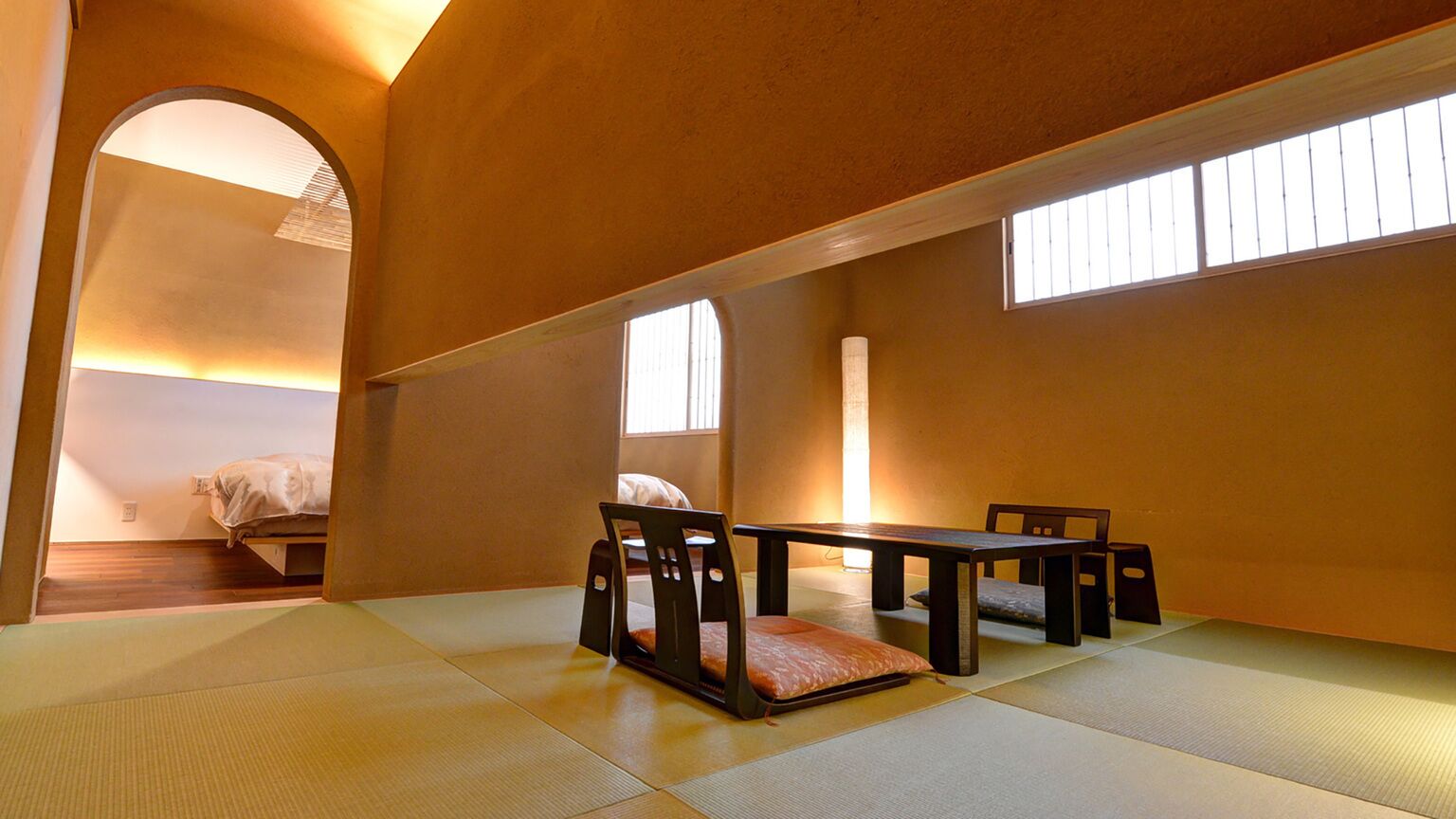 A traditional Japanese room with tatami flooring, a low table, chairs, and a bed.