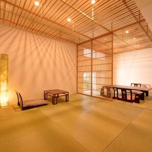 Una habitación tradicional japonesa con suelo de tatami, una mesa baja con sillas y una puerta corredera.
