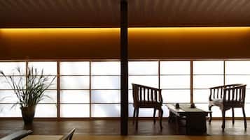 A traditional Japanese room with tatami flooring, a low table, two wooden chairs, and a potted plant.