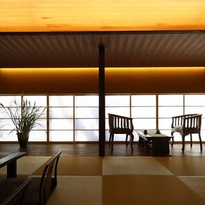 Una habitación japonesa tradicional con suelo de tatami, una mesita baja, dos sillas de madera y una planta en maceta.