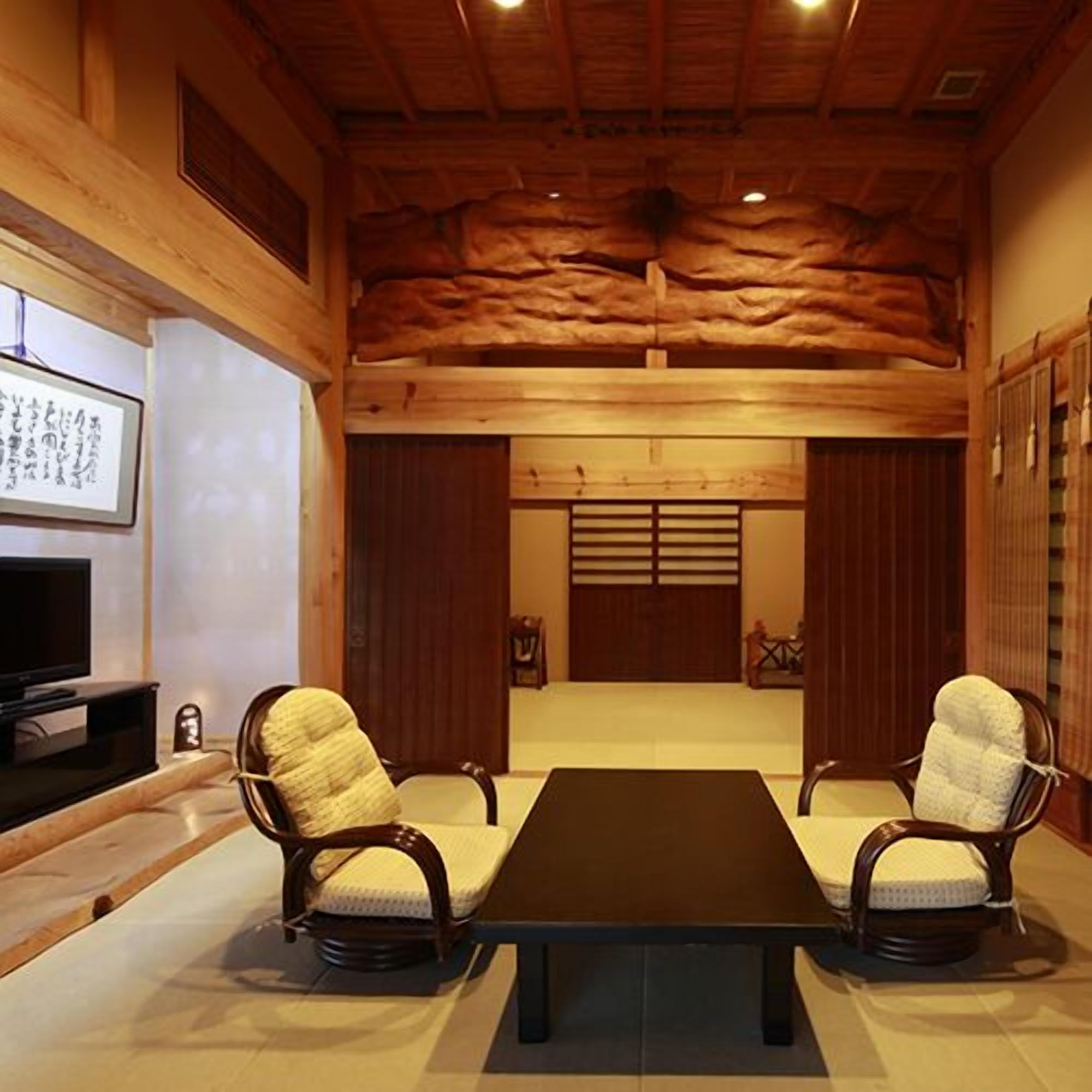 A room with a wooden ceiling, two chairs, a table, a TV, and a sliding door.