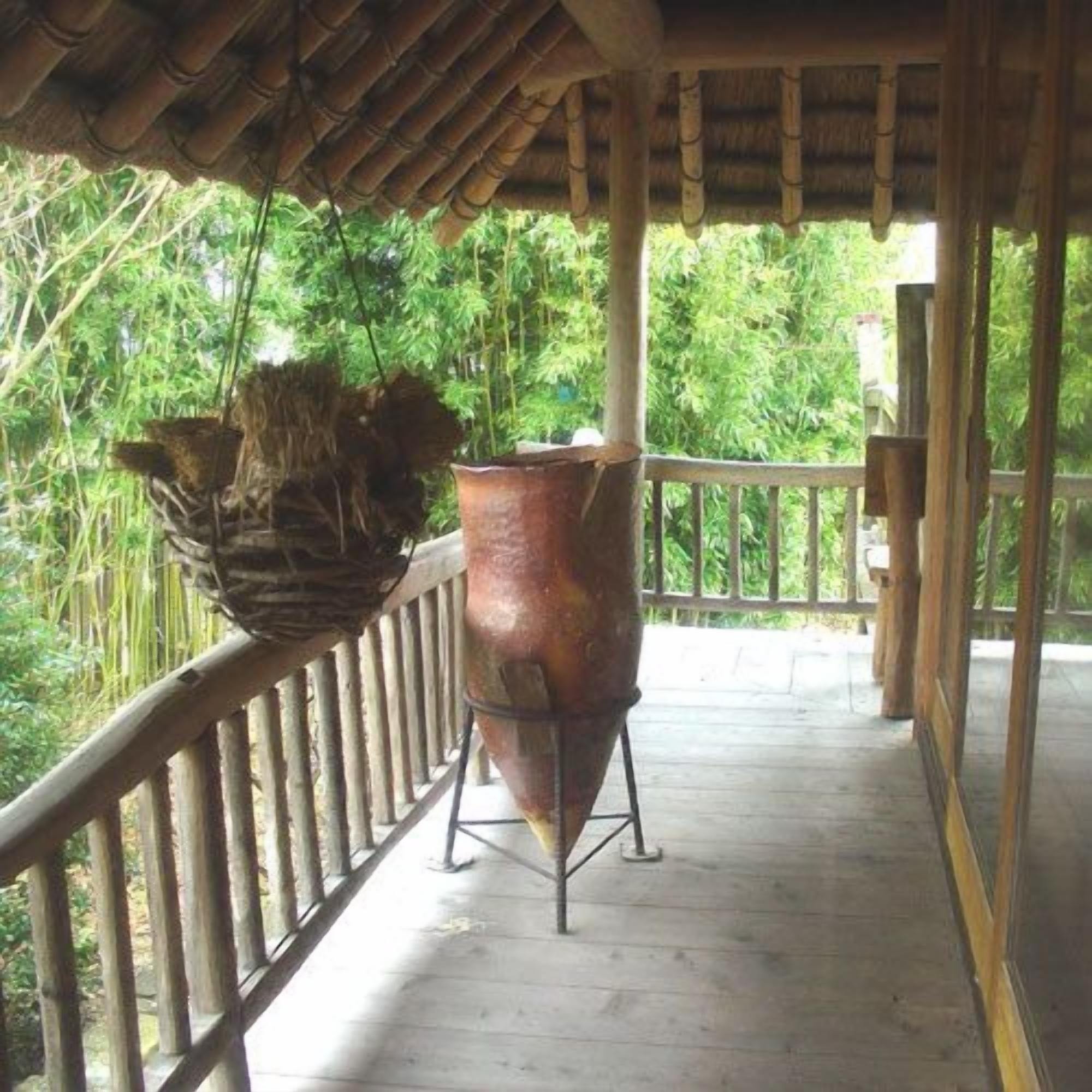 Un balcón de madera con barandilla de metal, una maceta colgante y una olla de cobre grande.