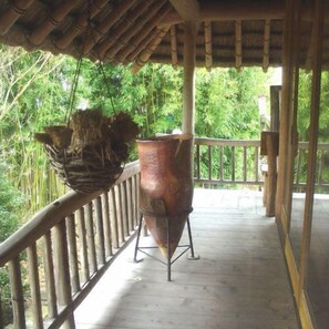 Un balcón de madera con barandilla de metal, una maceta colgante y una olla de cobre grande.
