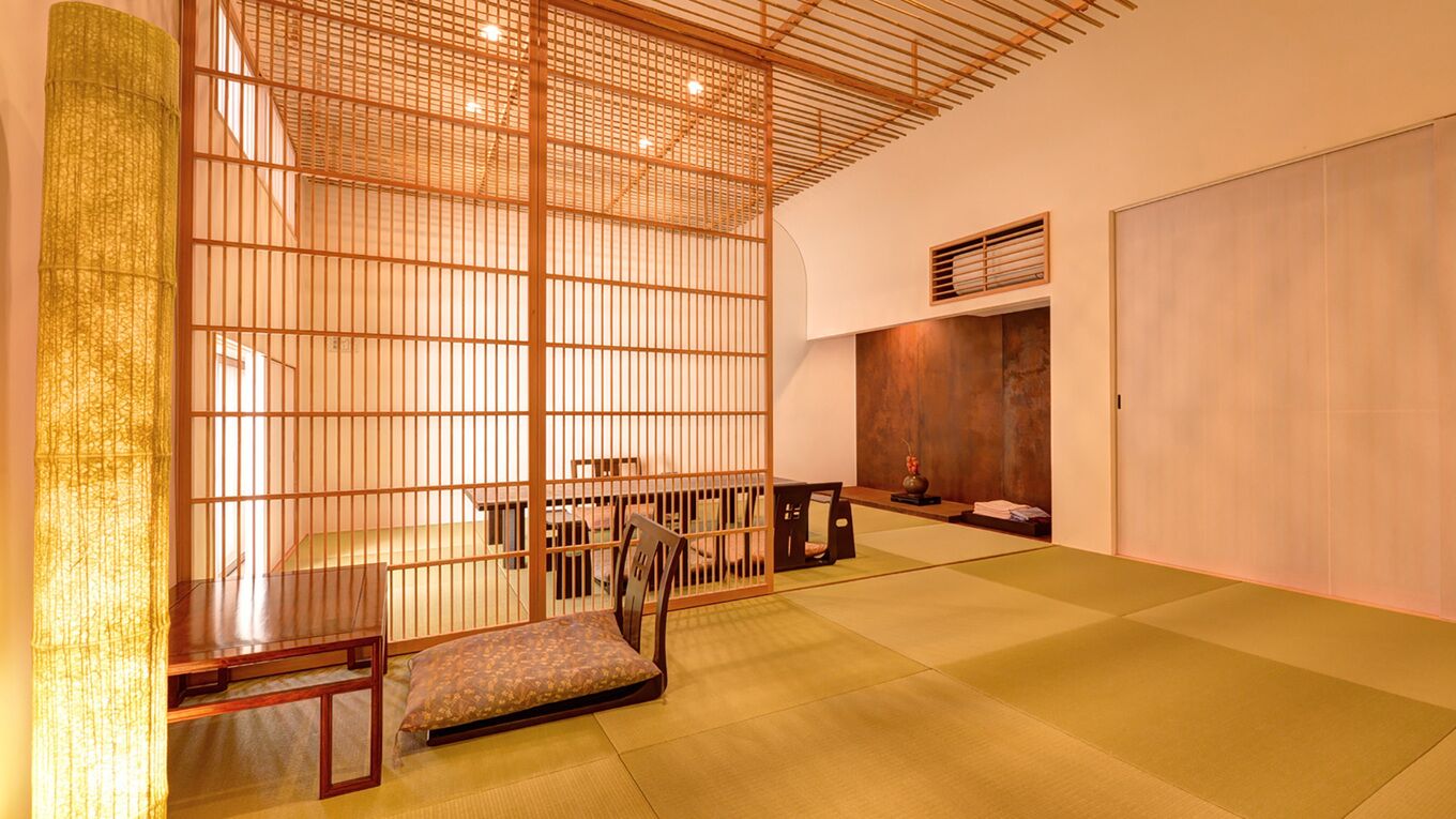 Una habitación tradicional japonesa con suelo de tatami, una mesa de madera baja, un banco acolchado y un puertas correderas.