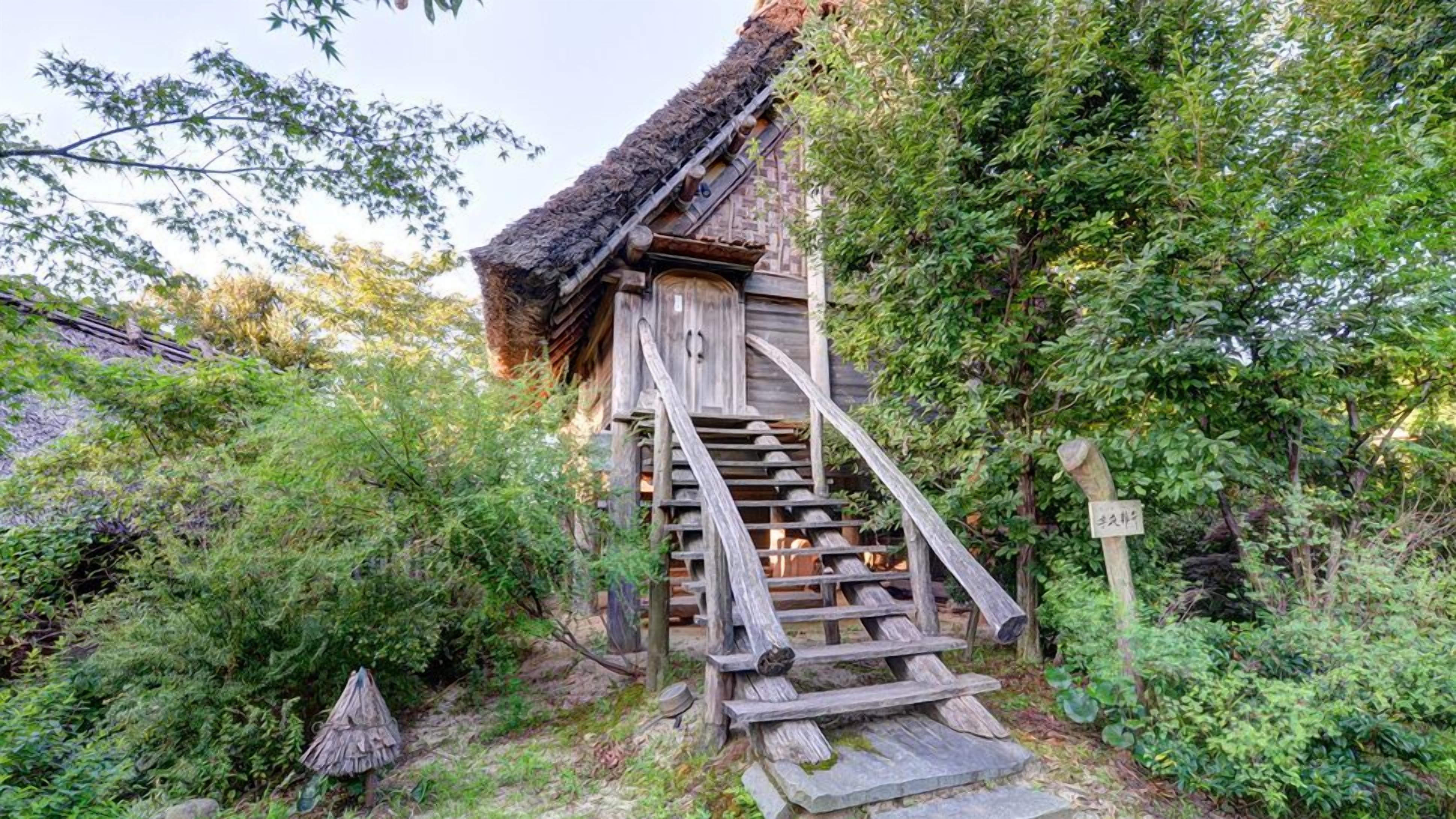A traditional wooden staircase leading to a thatched-roof building surrounded by dense greenery.