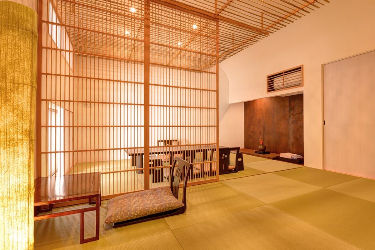 Una habitación tradicional japonesa con suelo de tatami, una mesa de madera baja, un banco acolchado y un puertas correderas.