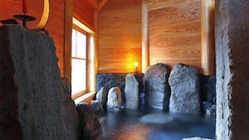 A wooden interior with a stone hot tub, a candle, and a window.